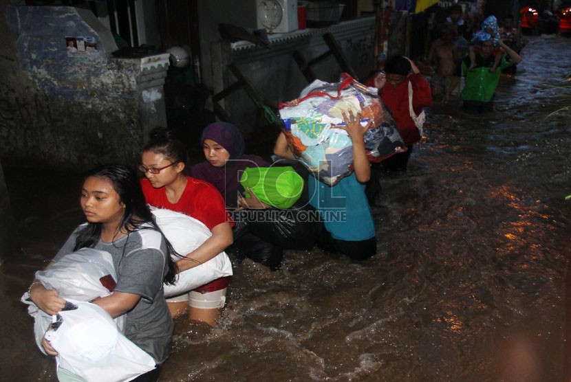   Warga menyelamatkan barang-barangnya ketika melintasi banjir yang merendam kawasan Kampung Pulo, Jakarta, Ahad (12/1).   (Republika/Yasin Habibi)