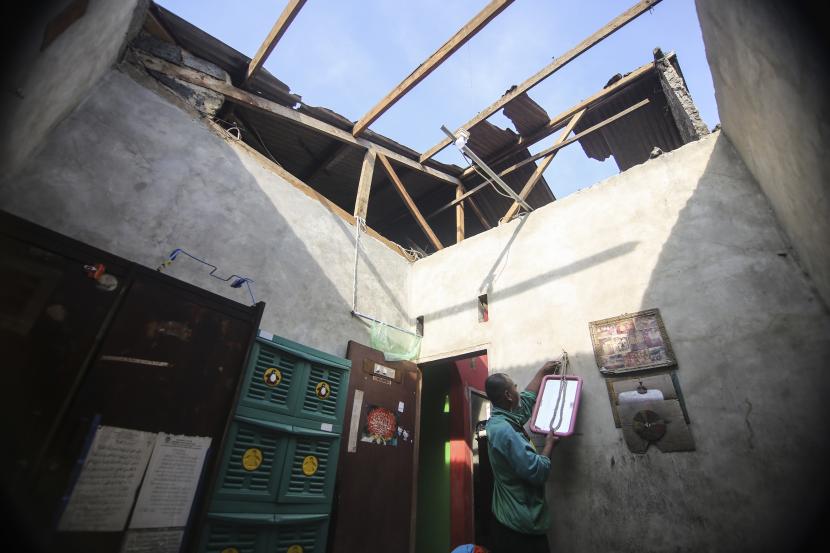 Warga merapikan barang-barang yang tertimpa atap rumah akibat angin kencang (Ilustrasi)