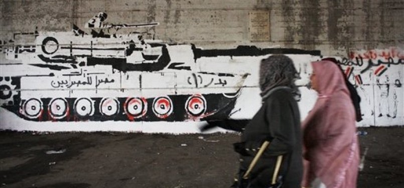 Warga Mesir melintas di depan sebuah dinding yang dihiasi grafiti yang menggambarkan tank militer karya Gazneer alias Mohamed Fahmy.