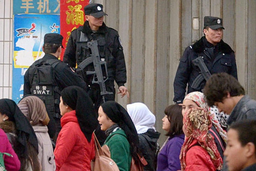 Warga Muslim Uighur berjalan melintas di depan tentara yang berjaga di kawasan Xinjiang Cina.