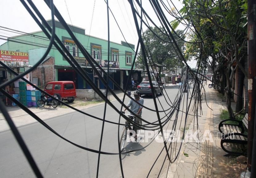 Warga naik sepeda melintas di depan instalasi kabel yang semrawut di Kampung Utan Ciputat, Tangerang Selatan, Banten, Senin (27/9/2021). 