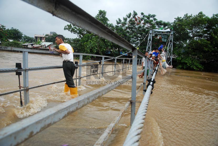 Warga nekat menyeberangi jembatan gantung Jati Pulo yang mulai terendam luapan Banjir Kanal Barat di Kecamatan Pal Merah, Jakarta Barat, Sabtu (18/1).  (Republika/Rakhmawaty La'lang)