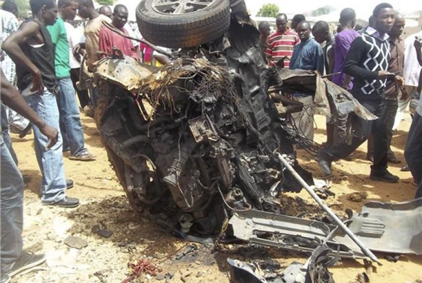 Warga Nigeria menyaksikan bangkai mobil yang hangus usai digunakan untuk aksi bom bunuh diri di dekat sebuah gereja di Yelwa, Bauchi, Nigeria, Ahad (3/6).