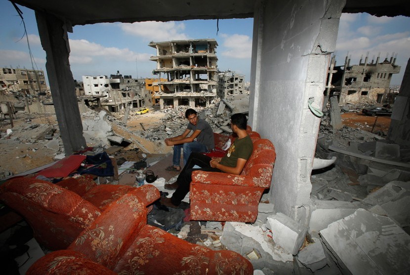 Warga Palestina berbincang santai di reruntuhan rumah akibat agresi Israel..