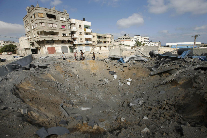 Warga Palestina berdiri di dekat lubang besar akibat serangan udara Israel di Kota Gaza, Palestina, Kamis (3/7)  