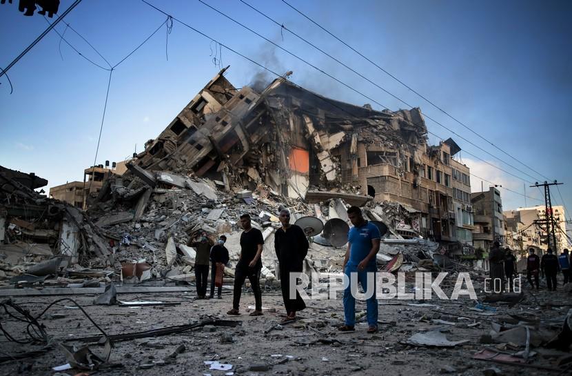 Warga Palestina berjalan di samping sisa-sisa bangunan 15 lantai yang hancur setelah terkena serangan udara Israel di Kota Gaza, Kamis (13/5).