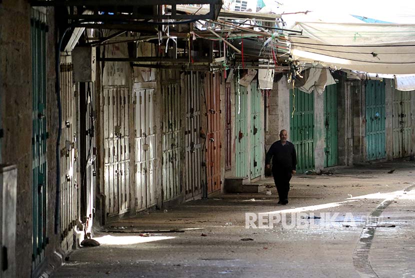 Warga Palestina berjalan melintasi pertokokoan yang tutup sebagai aksi  mogok massal di Kota Hebron, Tepi Barat, Palestina.