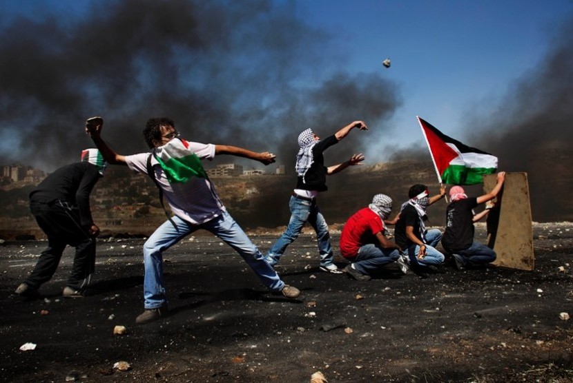  Warga Palestina melempar dengan batu kearah pasukan penjajah Israel dalam bentrokan yang terjadi saat memperingati 64 Tahun Hari Nakba dekat kota Ramallah di Tepi Barat Palestina, Selasa (15/5).  (Bernat Armangue/AP)
