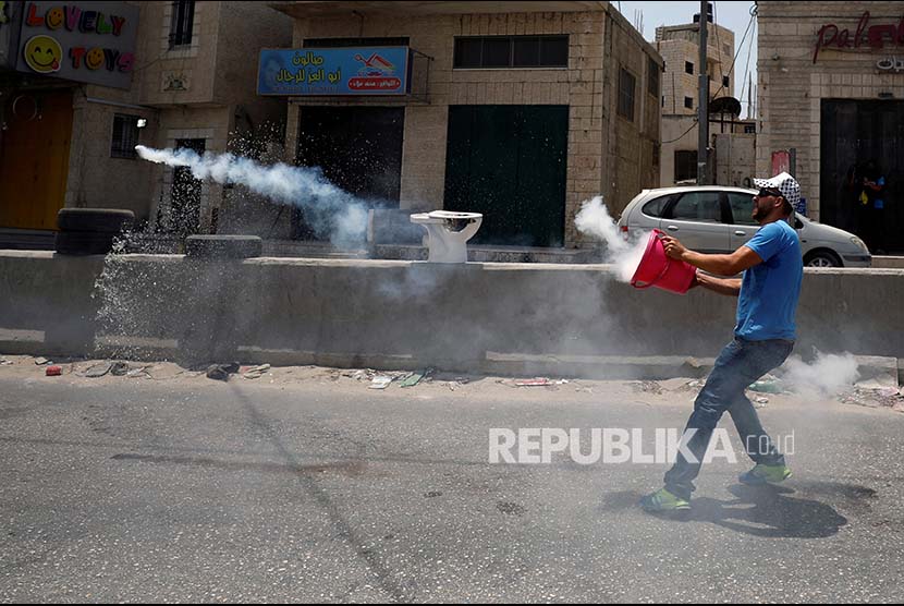 Warga Palestina melemparkan kembali kanister gas airmata ke arah polisi Israel di pos pemeriksaan Qalandiya di Kota Ramallah, Tepi Barat.