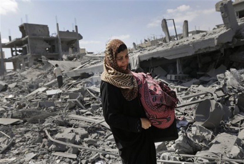 Warga Palestina membawa barang miliknya yang tersisa melewati reruntuhan rumahnya yang dihancurkan serdadu Israel, Sabtu (26/7).