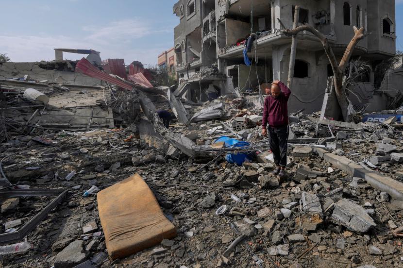 Warga Palestina memeriksa puing-puing bangunan yang hancur akibat serangan Israel di kamp pengungsi Maghazi, Jalur Gaza Tengah.