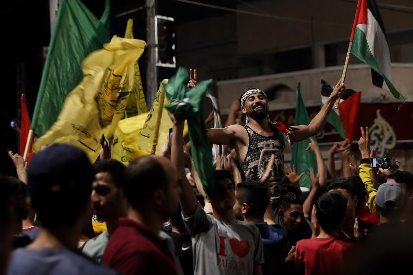 Warga Palestina menari saat mereka mengibarkan Hamas hijau dan bendera nasional mereka saat merayakan perjanjian gencatan senjata antara Israel dan Hamas di Kota Gaza, Jumat dini hari, 21 Mei 2021.