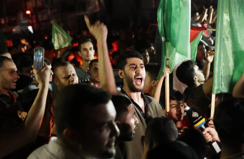  Warga Palestina meneriakkan slogan-slogan saat mereka mengibarkan Hamas hijau dan bendera nasional mereka saat merayakan perjanjian gencatan senjata antara Israel dan Hamas di Kota Gaza, Jumat pagi, 21 Mei 2021. 