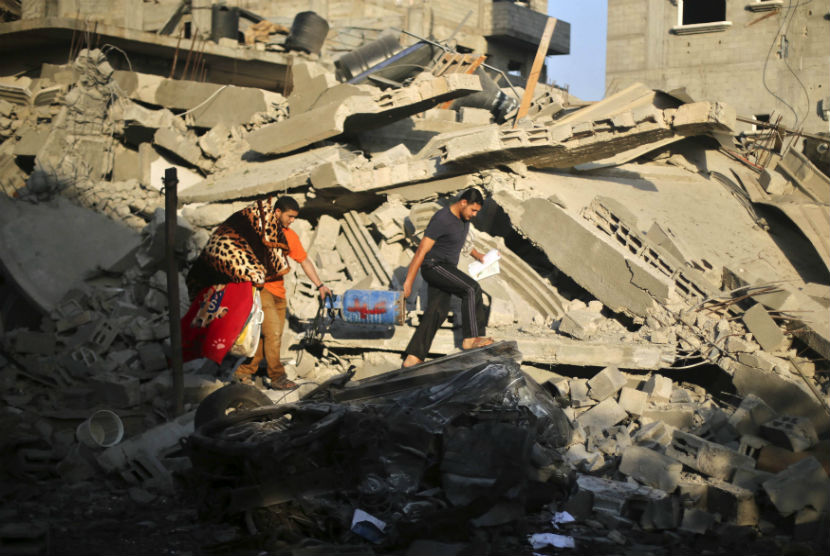Warga Palestina menggotong tabung gas dari reruntuhan rumah yang hancur terkena serangan udara Israel di Gaza pada Kamis (10/7). 