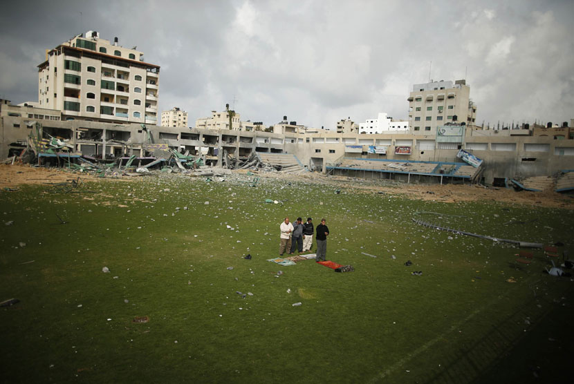 Warga Palestina shalat di tengah lapangan stadion sepak bola, yang hancur akibat serangan udara Israel selama konflik delapan hari di Kota Gaza,Selasa (4/12)/ (Reuters/Suhaib Salem)