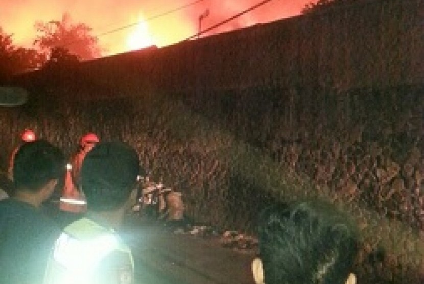 warga penyaksikan petugas pemadam menjikan api dalam kebakaran yang melanda sebuah gudang mebel di Jalan Industri Barat, Kelurahan Husein Sastranegara, Kecamatan Cicendo, Kota Bandung, pada Sabtu (25/11) dinihari. 