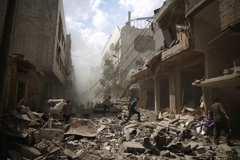 Warga Suriah berjalan di antara puing-puing bangunan setelah serangan udara dari pasukan rezim