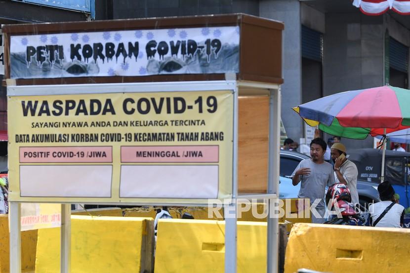 Warga tanpa mengenakan masker melintasi replika peti mati dan papan himbauan waspada COVID-19 di kawasan Pasar Tanah Abang, Jakarta, Selasa (1/9/2020). 