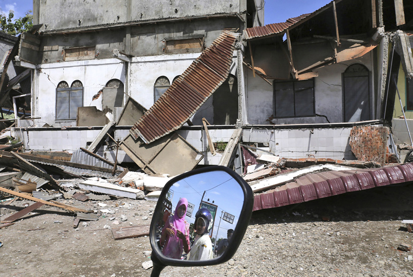 Warga terlihat dalam cermin sepeda motor saat mereka menyaksikan bangunan yang rusak setelah gempa di Pidie Jaya, Provinsi Aceh, Indonesia, Rabu, (7/12).