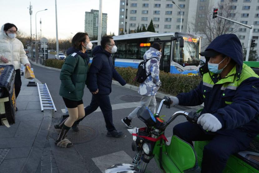 Warga yang memakai masker menyeberang jalan saat bus umum melintas di Beijing, Sabtu, 3 Desember 2022. Otoritas China pada Sabtu mengumumkan pelonggaran lebih lanjut pembatasan COVID-19 dengan kota-kota besar seperti Shenzhen dan Beijing tidak lagi mewajibkan tes negatif untuk naik kendaraan umum.