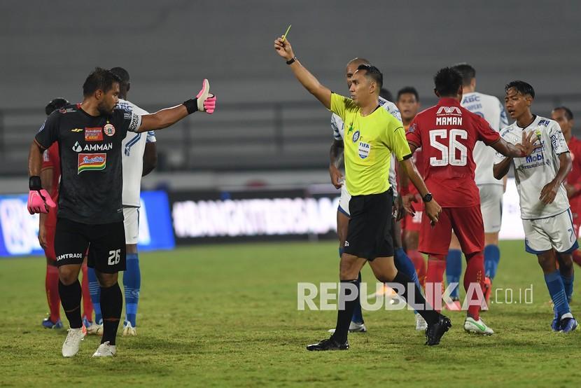 Wasit Fariq Hitaba (ketiga kanan) memberikan kartu kuning kepada penjaga gawang Persija Jakarta Andritany (kiri) setelah terlibat keributan dengan pemain Persib Bandung dalam pertandingan sepak bola Liga 1 di Stadion I Wayan Dipta, Gianyar, Bali, Selasa (1/3/2022). Persib Bandung memenangkan pertandingan dengan skor 2-0.