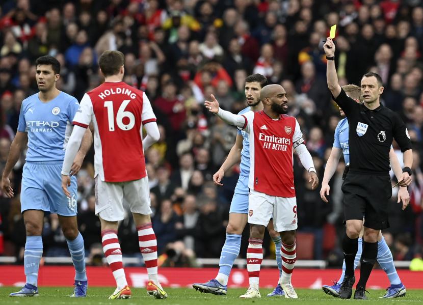 Wasit Stuart Attwell menunjukkan kartu kuning kepada Rob Holding (2-kanan) dari Arsenal selama pertandingan Liga Primer Inggris antara Arsenal dan Manchester City di London, Inggris, 01 Januari 2022. Arsenal kalah 1-2 di laga itu.