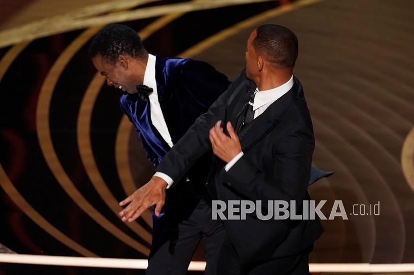  Will Smith (kanan) menampar presenter Chris Rock di atas panggung saat mempersembahkan penghargaan untuk Film Dokumenter Terbaik di Oscar pada Ahad 27 Maret 2022, di Dolby Theatre di Los Angeles, AS. Smith yang tadinya ikut tertawa naik pitam beberapa detik setelah mendengar lelucon Rock tentang kepala plontos istrinya.  