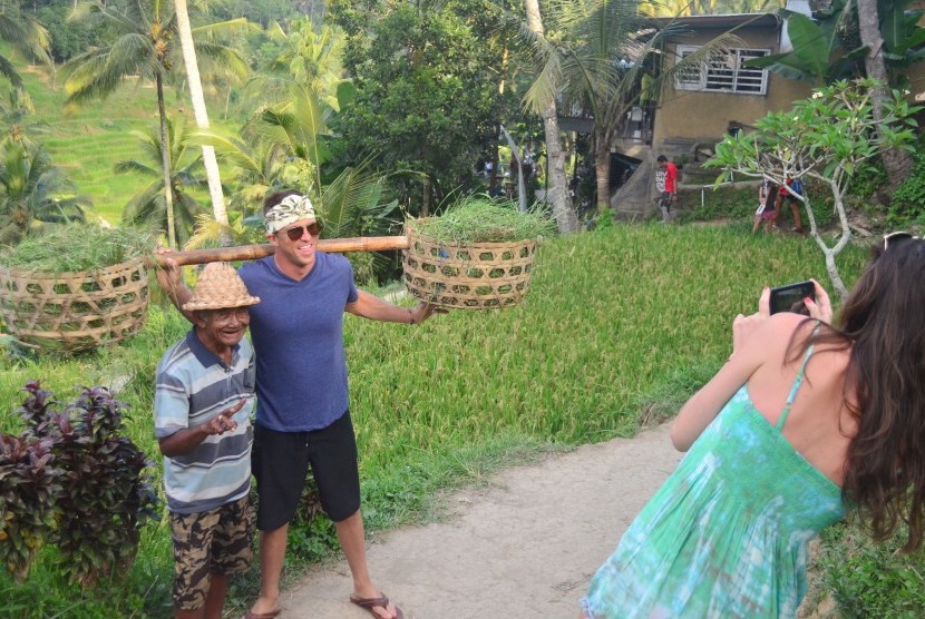 Wisatawan asing berfoto dengan warga setempat di kawasan objek wisata pemandangan pedesaan dengan sawah berundak (terasering) di Ceking, Tegalalang, Gianyar, Bali. Jaga kesehatan selama liburan sangat penting.