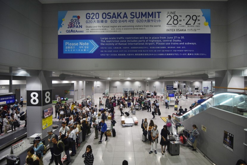 Wisatawan beraktivitas di bawah spanduk pengumuman pengalihan arus saat Pertemuan G20 mendatang, di Bandara Internasional Kansai, Osaka, Jepang, Senin (24/6/2019). 