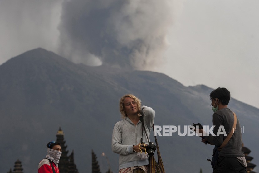 Wisatawan beraktivitas di Pura Besakih yang berlatar belakang Gunung Agung meletus di Karangasem, Bali, Selasa (28/11).