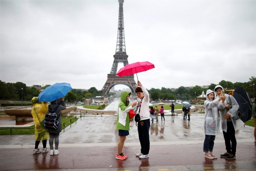 Wisatawan berfoto di pelantaran Trocadero dengan latar pemandangan Menara Eiffel saat hujan mengguyur Paris, Prancis. Pariwisata Uni Eropa pulih lebih cepat daripada tempat lain karena sertifikat vaksin. Ilustrasi. 