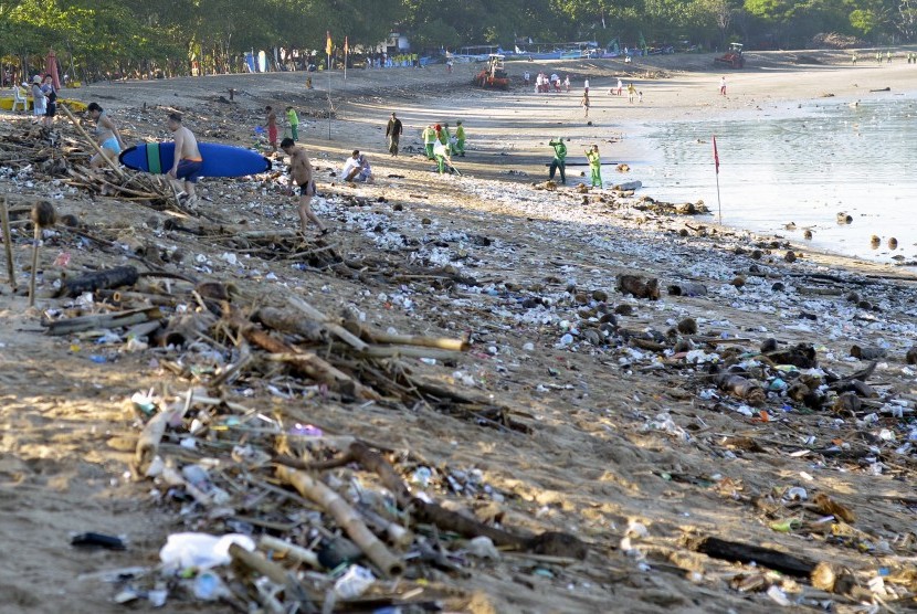 Wisatawan berjalan di antara tumpukan sampah yang terdampar di Pantai Kuta, Bali, Senin (15/2).