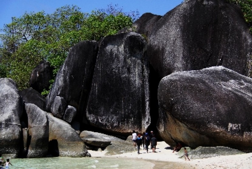 Wisatawan berjalan di tepi pantai di antara bebatuan granit di Tanjung Tinggi, Belitung, Bangka Belitung.