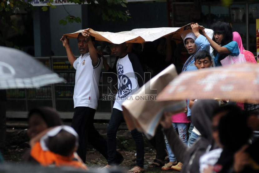  Wisatawan berlindung dari hujan dengan menggunakan alat seadanya saat berkunjung ke Kebun Binatang Ragunan, Jakarta, Selasa (25/12). (Republika/Aditya Pradana Putra)