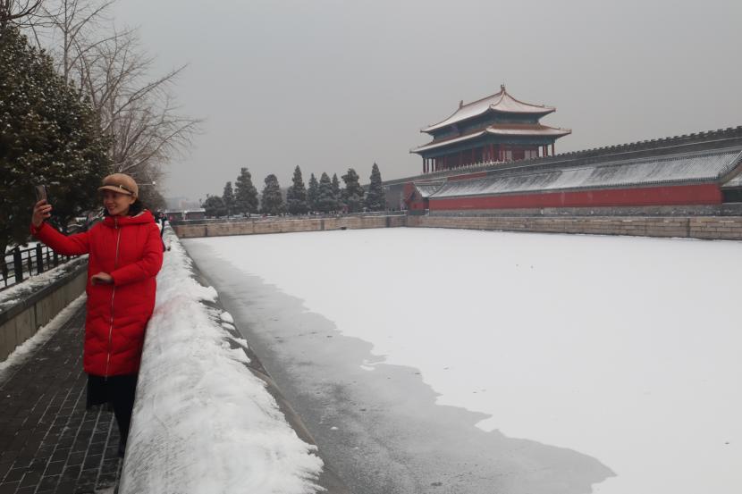 Wisatawan berswafoto dengan latar belakang sungai yang bersalju dan pintu gerbang Istana Kota Terlarang, Beijing, China, Sabtu (22/1/2022). 