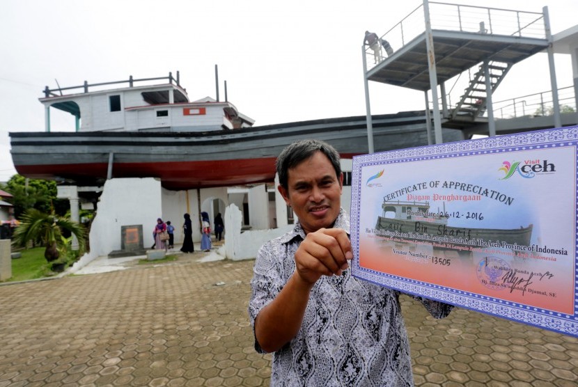 Wisatawan mancanegara asal Malaysia memperlihatkan sertifikat yang diperoleh seusai mengunjungi situs tsunami kapal di atas rumah pada hari peringatan 12 tahun bencana gempa dan tsunami di Banda Aceh, Aceh, Senin (26/12). 