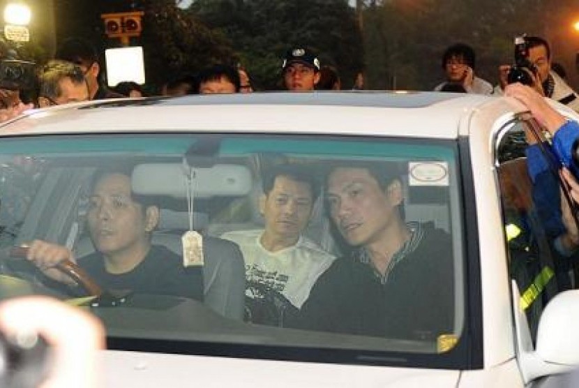 Won Kuok Kai (berkaos putih) duduk di belakang mobil yang dikelilingi wartawan.
