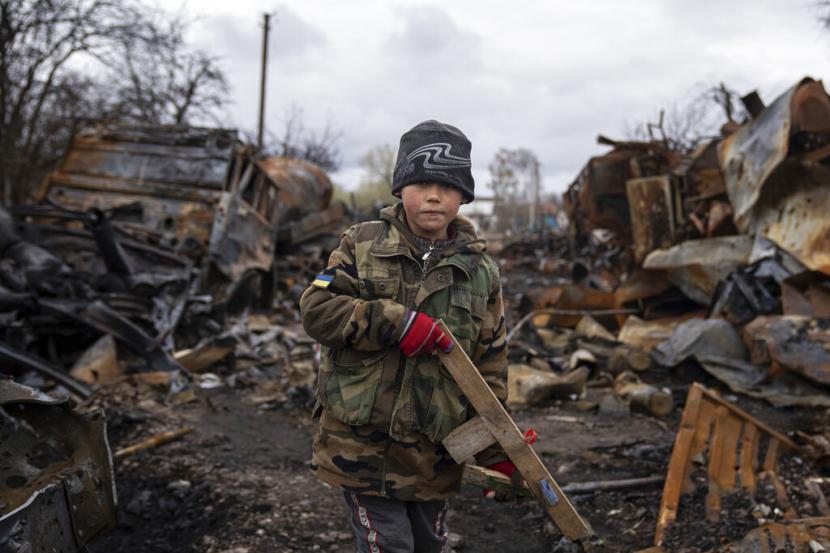 Yehor, 7, memegang senapan mainan di samping kendaraan militer Rusia yang hancur di dekat Chernihiv, Ukraina, Ahad, 17 April 2022.