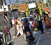 Petugas kepolisian membantu pengguna jalan yang akan menyeberang di pasar Gebang, Cirebon, Jawa Barat.