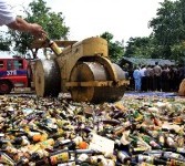 Petugas menggunakan alat berat memusnahkan ribuan botol minuman keras (miras). 