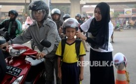 (ILUSTRASI) Petugas memasangkan helm kepada anak yang diajak berkendara.