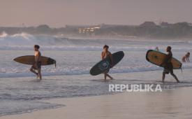Sejumlah wisatawan membawa papan selancar berjalan menuju ke tengah laut saat berlibur di Pantai Kuta, Badung, Bali.