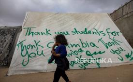 Seorang anak pengungsi Palestina berjalan melewati tenda dengan pesan terima kasih yang didedikasikan untuk mahasiswa Universitas Columbia di New York, AS, di kamp pengungsi Rafah di Jalur Gaza. 