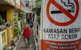 Warga berjalan dengan latar depan poster informasi kawasan bebas asap rokok di permukiman padat penduduk di Kayu Manis, Matraman, Jakarta, Rabu (22/11/2023). Merokok bahkan sesekali atau dalam jumlah sedikit tetap memberikan kerusakan berulang pada sel-sel paru-paru.