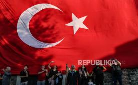 Orang-orang yang berdiri di depan bendera raksasa Turki menyaksikan pilot militer Turki dari formasi Bintang Turki tampil saat perayaan 100 tahun Republik Turki di Istanbul, Turki, Ahad (29/10/2023).