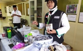 Petugas Perlindungan Jamaah (Linjam) Eva Widiastuti, menunjukkan sejumlah barang yang disita dari jamaah haji asal Embarkasi Surabaya, Jumat (12/7). Barang-barang yang disita antara lain, rokok, jamu kuat, sari rapet, dan lainnya. 