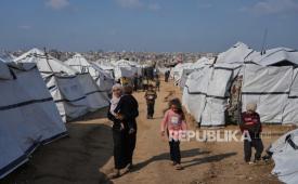 Seorang wanita Palestina menggendong seorang anak saat mereka berjalan di sepanjang tenda yang didirikan untuk pengungsi di Kota Gaza, Rabu, 17 Desember 2025.