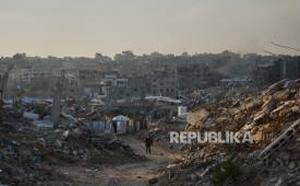 Warga Palestina berjalan di sepanjang jalan yang dikelilingi oleh bangunan yang hancur selama operasi udara dan darat Israel di lingkungan Sheikh Radwan, di Kota Gaza, Selasa, 30 Desember 2025.