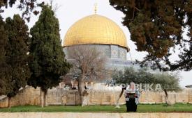 Seorang perempuan membaca Alquran dengan latar belakang Dome of Rock, kompleks Masjid Al Aqsa, Palestina.