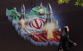 Seorang warga Iran berjalan melewati spanduk anti-Israel yang memuat gambar rudal Iran, di Teheran, Iran.